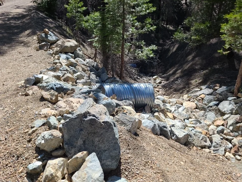 A road culvert opening surrounded by rock that protects the drainage outlet